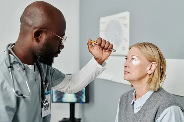 In a medical office, a male ophthalmologist uses a pen light to examine the eyes of a woman.