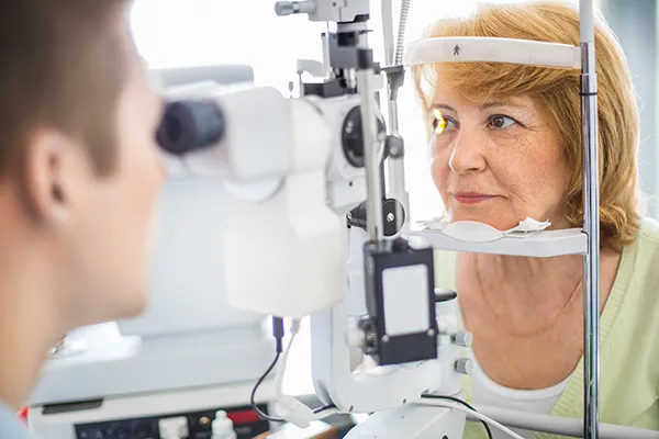 A woman with ginger hair sits behind a slit lamp while having her eyes examined at an ophthalmologist’s office