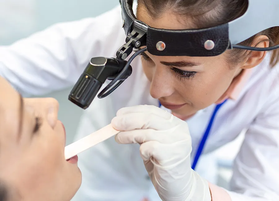 A doctor examines a patient's throat using a light and a tongue depressor