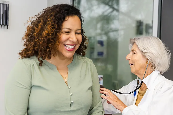 A mature woman doctor is using a stethoscope to listen to the lungs of a younger woman patient