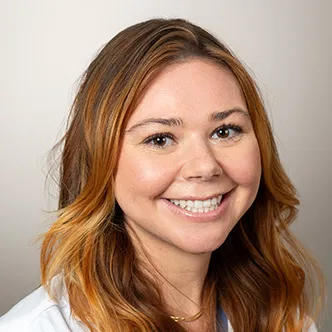 Ms. Burchett has long wavy red hair, is wearing a white medical coat, and is smiling at the camera