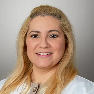 Allita Chaplinskiy has long blonde hair, wears a white medical coat, and is smiling at the camera.