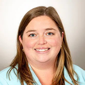 Dr. Dawson has long dark blonde hair, is wearing a light blue blouse, and is smiling at the camera