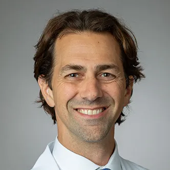 Dr. DiSandro has short brown hair and is wearing a white shirt and silver and blue tie under a white medical coat.