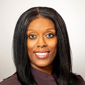 Kimberly Gray has long dark hair, is wearing a burgundy medical jacket, and is smiling at the camera.