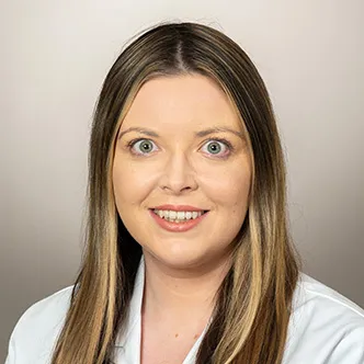 Dr. Horgan has long, straight light brown hair, is wearing a white medical coat, and is smiling at the camera