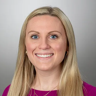 Sara Jorgensen has long blonde hair, is wearing a magenta top, and is smiling at the camera
