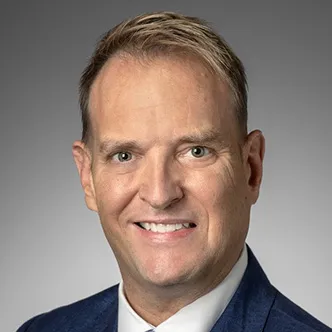 Mr. Lively has short blond hair, is wearing a dark suit and is smiling at the camera.