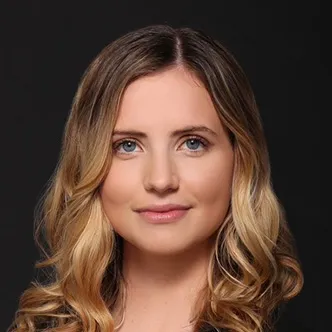Eladra Ludvigsen has long blonde wavy hair, is wearing a black shirt, and is looking at the camera.