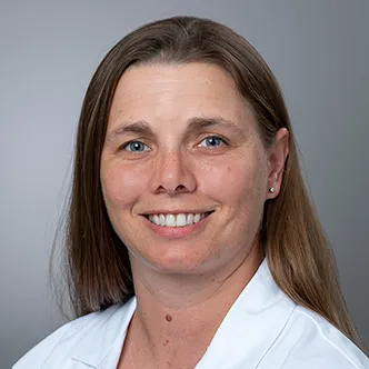 Dr. Ringwood has long, medium brown hair, is wearing a white medical coat, and is smiling at the camera.