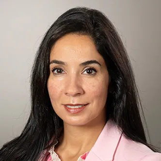 Dr. Saber has long dark hair, is wearing a multi-pink blouse under a pink blazer, and is smiling at the camera.