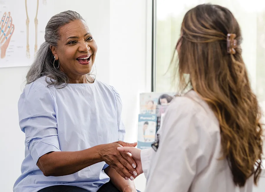 A patient smiles and shakes hands with her doctor.