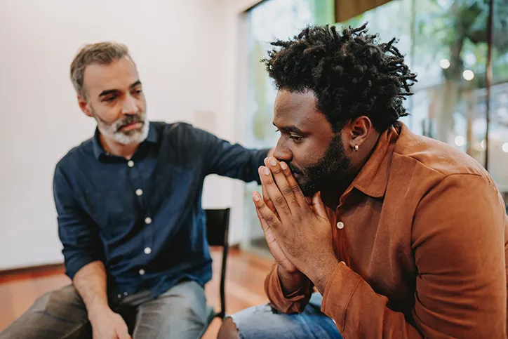 A black man in a dark orange shirt seeks counseling in a therapy group