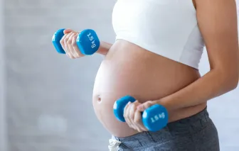 Pregnant woman doing exercise with dumbbells at home.