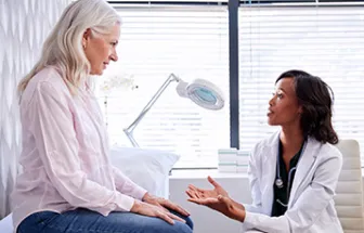a senior woman sits on exam table in doctor's office during an exam