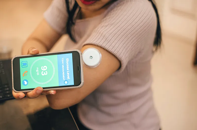 Woman with continuous glucose monitoring on arm and cell phone reading results