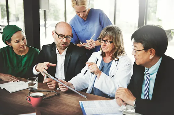 Five medical professionals talk together during a meeting.
