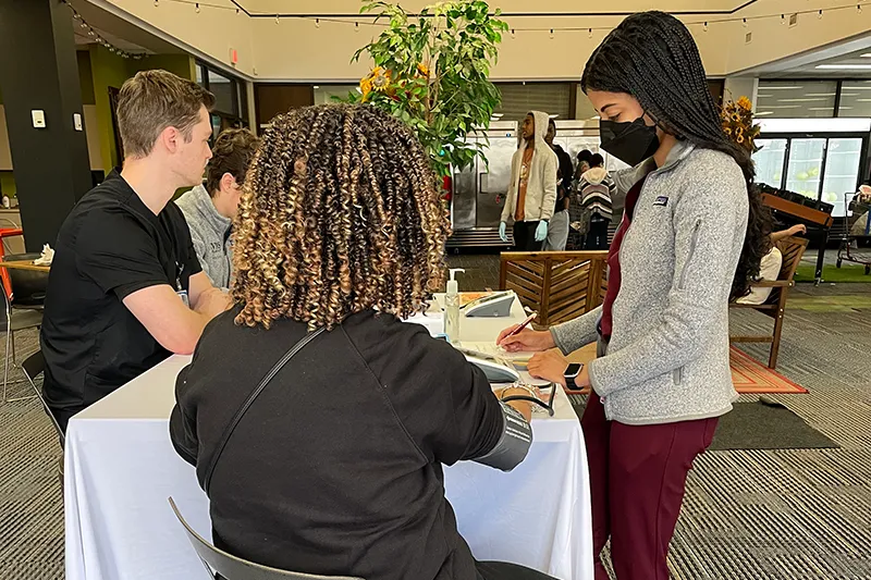students providing blood pressure screenings at a table.