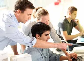 An instructor works with students on a computer.