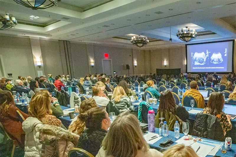 conference room with hundreds of people sitting looking at an ultrasound on a screen.