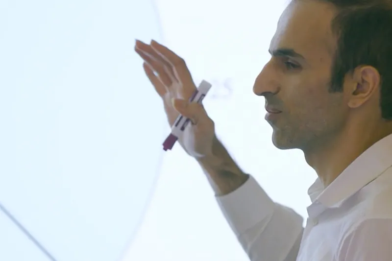 A man in a white button down shirt giving a presentation in a classroom
