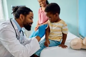 Masked pediatrician with masked mom and baby on lap