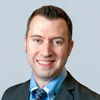 Dr. Smith has short dark hair, is wearing a blue shirt and white shirt under a gray suit jacket with blue and gray necktie. He is smiling at the camera.