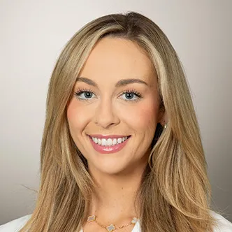Ms. Simokaitis has long blond hair, is wearing a white medical coat, and is smiling at the camera