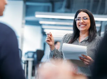 Woman speaking to a group with a smile and a pen in her hand