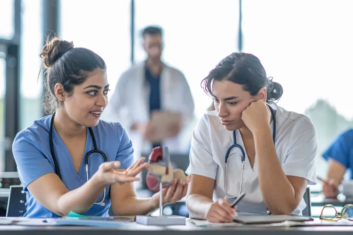 2 medical students talking in a classroom with a fake heart model.