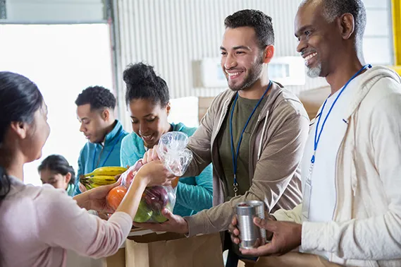 Smiling volunteers fill brown paper bags with fruit for a food pantry client.