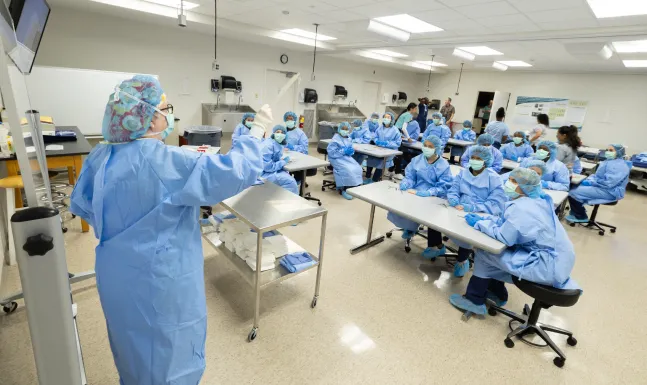 A classroom full of HSA students in blue lab coats and masks.