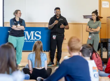 3 healthcare professionals giving a speech in front of students