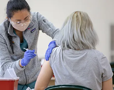 A female medical professional administered a COVID-19 vaccination to a person with long white hair