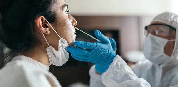 Doctor in protective workwear taking nose swab test from young woman