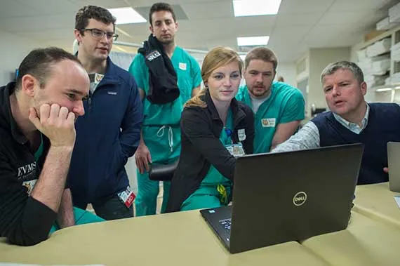 Students and faculty gather around a computer during a lesson.