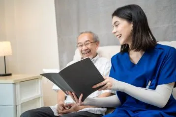 Doctor sharing a book with older Asian man in a hospital bed