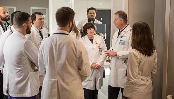 A doctor speaks with several residents in a medical hallway