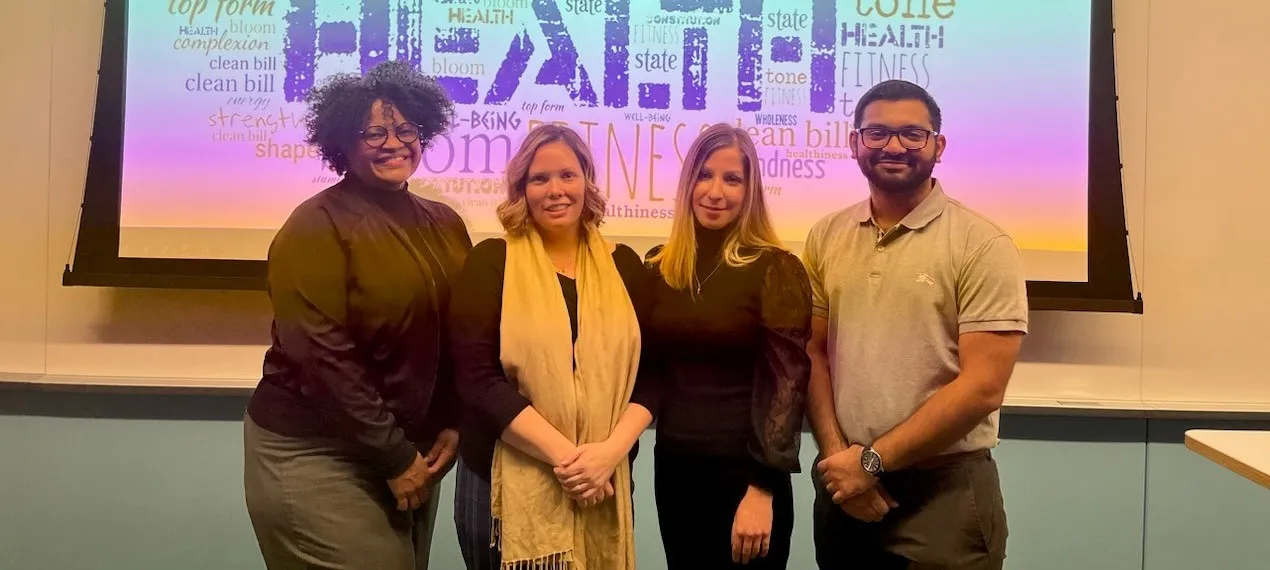 Four students stand in front of a multi colored poster facing the camera
