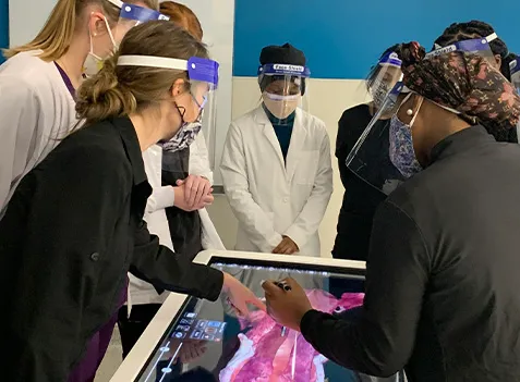A group of students wearing masks and face shields standing around a table.