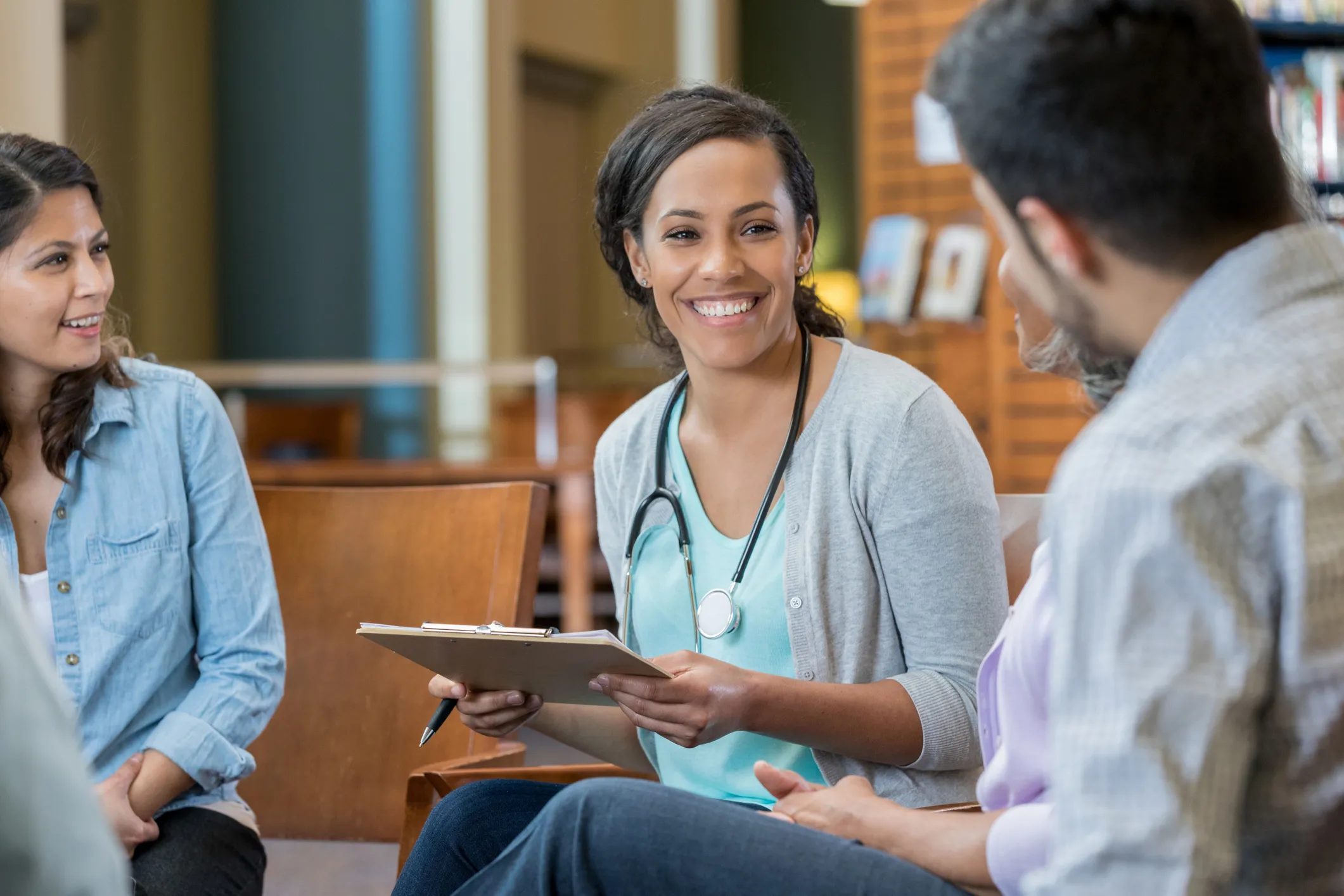 A young female medical instructor sits in a circle with her students in a library.
