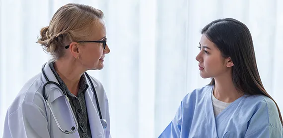 Physician Assistant in a white coat and wearing glasses with female patient in gown