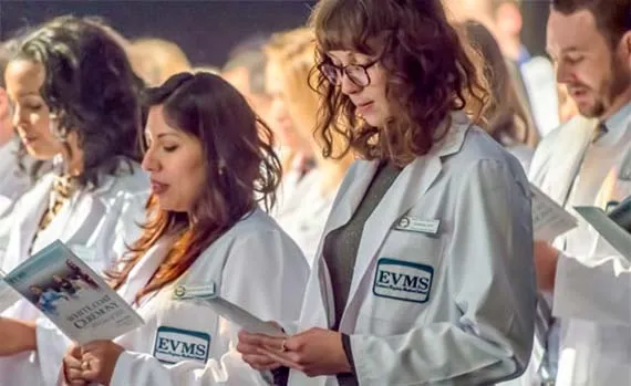Students wearing white medical coats with EVMS logos read together from their programs.