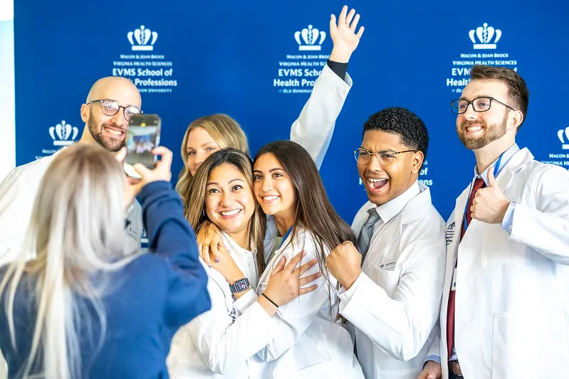 Students in white lab coats smiling as they have their photo taken