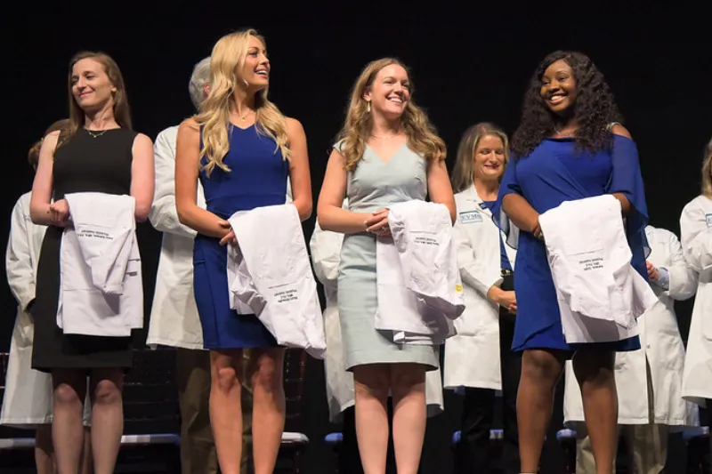 Female students hold white coats during annual Awards & White Coat Ceremony