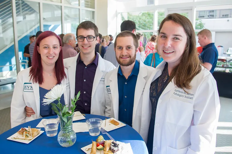 A group of Physicians' Assistant graduates wearing white coats smile during a reception