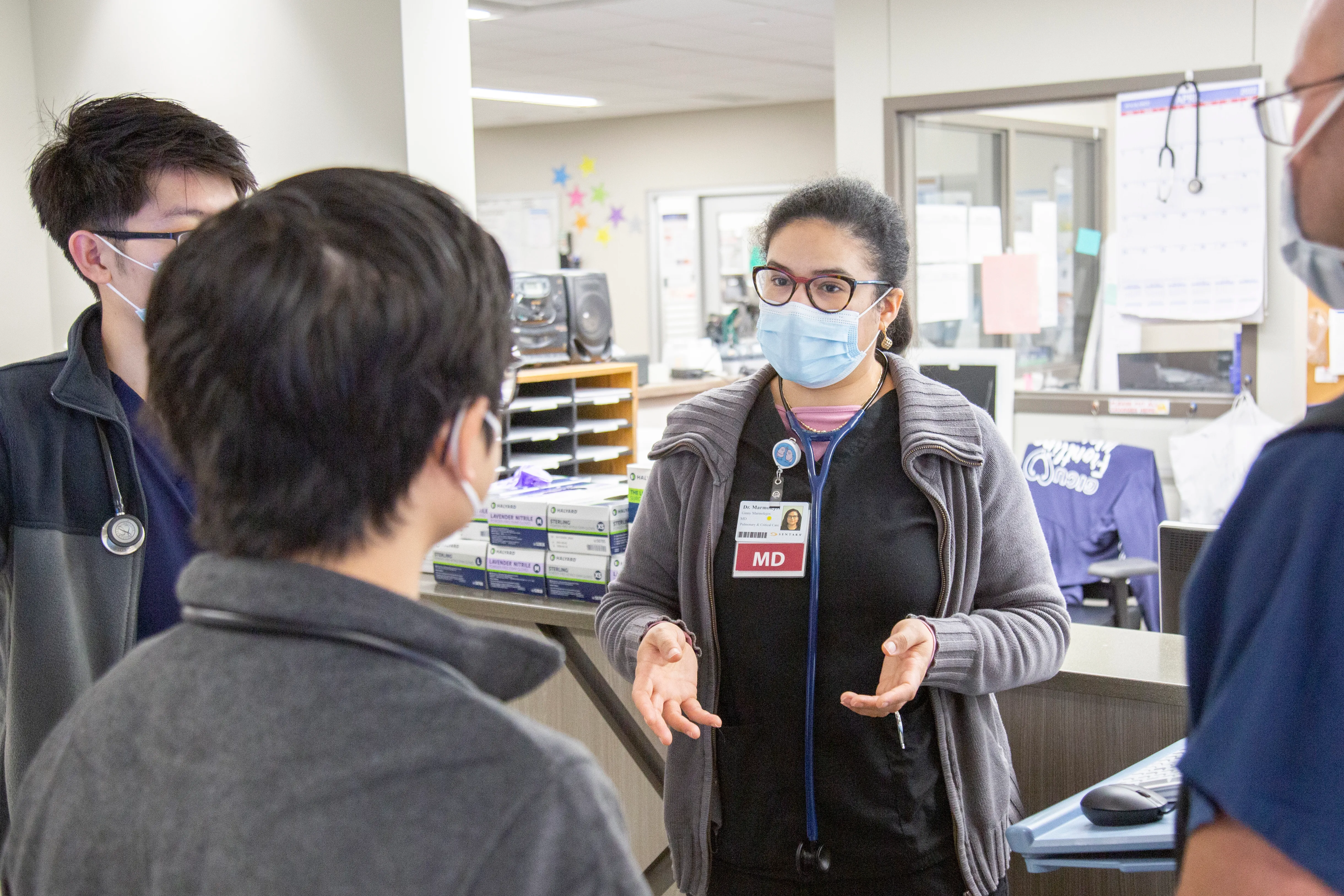 A female doctor explaining something to 3 other health care professionals with a mask.