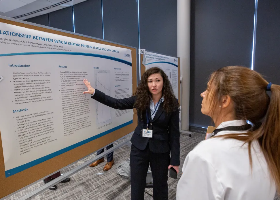 A female presenter is explaining a project poster to another individual.