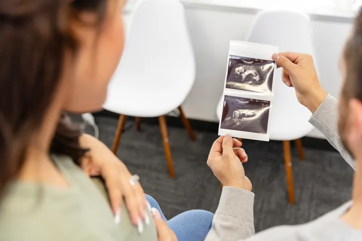 A view over the shoulders of an unrecognizable expectant couple looking at ultrasound photos