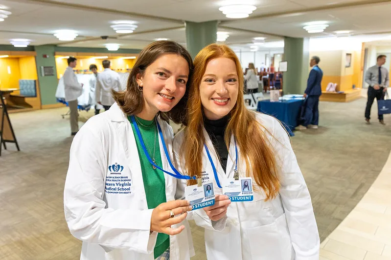Two students smiling in white coats at orientation.